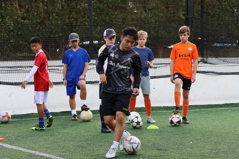 Children practising soccer dribbling and ball mastery at an outdoor training facility in Sydney, with multiple soccer balls